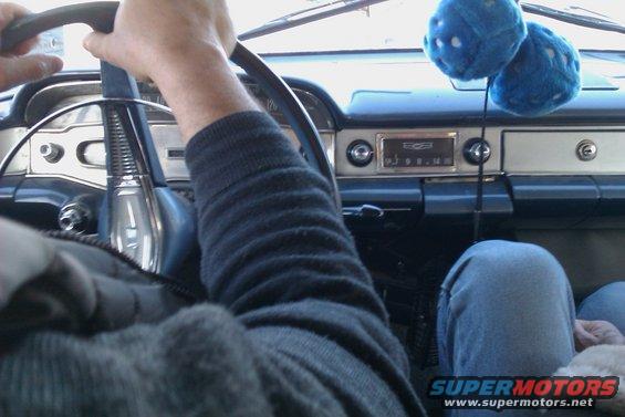 Interior view of a vintage car dashboard with fuzzy dice hanging from the rearview mirror