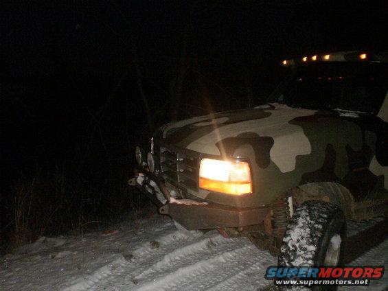 Camouflaged Ford truck with aftermarket bumper and auxiliary lights, parked in snow at night