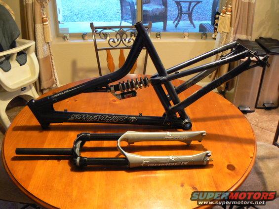 Black Santa Cruz bike frame and grey Marzocchi Bomber fork on wooden table