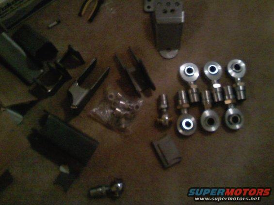 Assortment of metal automotive suspension components and tools scattered on a brown surface