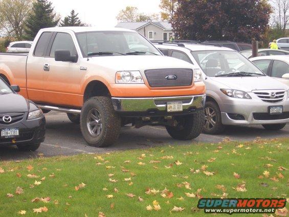 Lifted orange and white pickup truck parked next to a silver Mazda