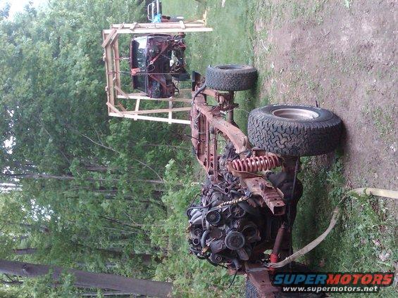 Truck chassis with engine and cab on a wooden frame, outdoors