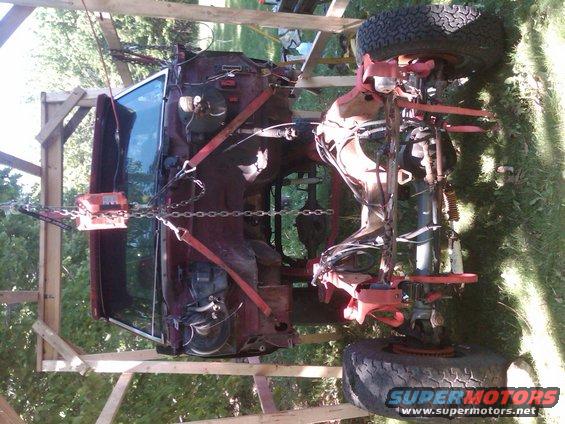 Truck body lifted and supported by wood frame and chains, showing underside and suspension