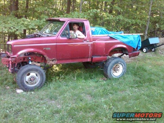1992 Ford F-150 pickup truck, red, with a man in the driver's seat. Front end is partially disassembled