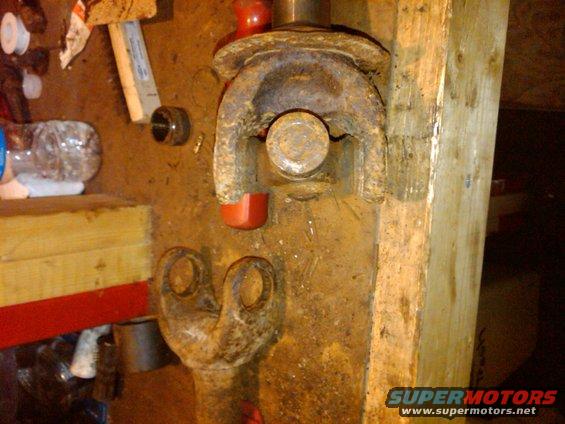 Close-up of a rusty driveshaft universal joint with red protective caps