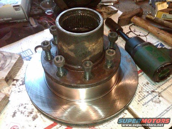 Wheel hub with six lug nuts and a brake rotor, on a workbench with tools