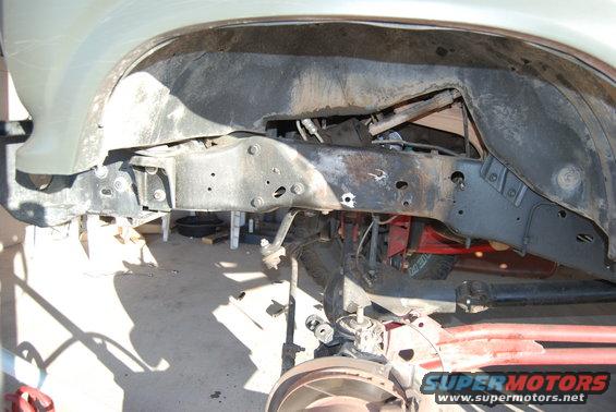 Underside view of vehicle frame and suspension parts, with a tire visible in the background. SuperMotors logo in lower right