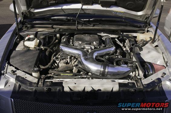 Engine bay with shiny metal intake pipes and a red air filter. Hood is up