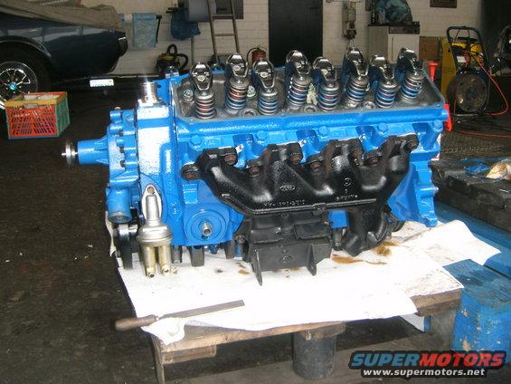 Blue engine with black exhaust manifolds on a workbench, with a file and oil stains