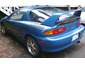 Blue 1993 Mazda MX-3 coupe with a rear spoiler and aftermarket wheels, seen from the rear-right