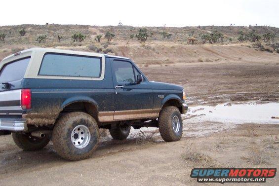 Dark green 1995 Ford Bronco with tan top and trim, off-road tires, in a muddy landscape