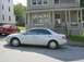 2003 Mazda 6 - A silver sedan is parked on the street in front of a house, with another red car behind it.