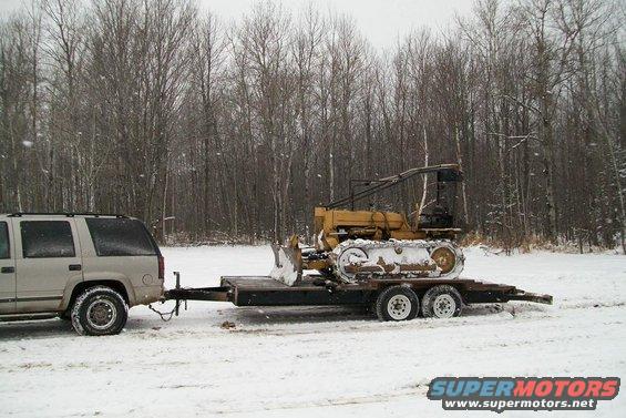 Yellow bulldozer on trailer towed by SUV in snow
