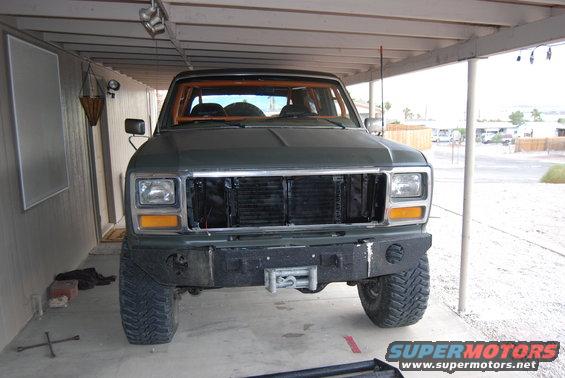 Green Ford Bronco with orange roll cage, aftermarket bumper, and winch. Front view
