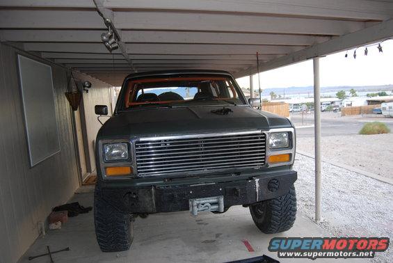 Dark green SUV front view with chrome grille, winch, and orange roll cage