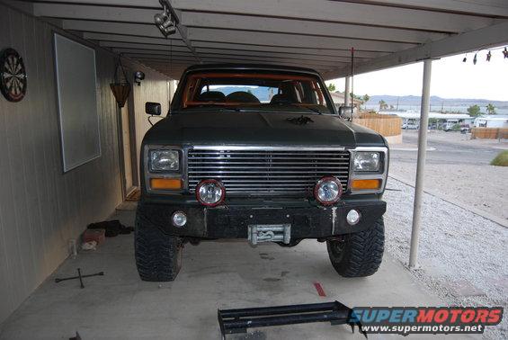 Dark green Ford Bronco front end with chrome grille, aftermarket bumper, and winch. Parked under a carport