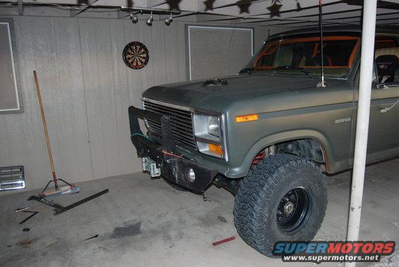 Green Ford Bronco with a large aftermarket bumper and off-road tires, parked in a garage