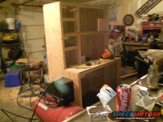 Garage scene with unfinished wooden cabinet, air compressor, and Coca-Cola can