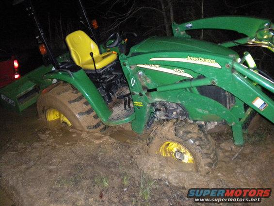 Green John Deere tractor stuck in mud, yellow seat, front loader, 4120 model designation