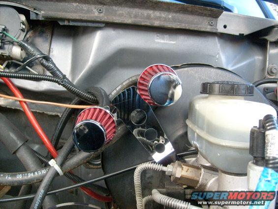 Engine bay with two red cone air filters and a chrome bracket. Brake fluid reservoir is visible