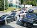 2003 Mazda 6 - Several cars are parked on a street, with people gathered around a dark sedan with its hood up.