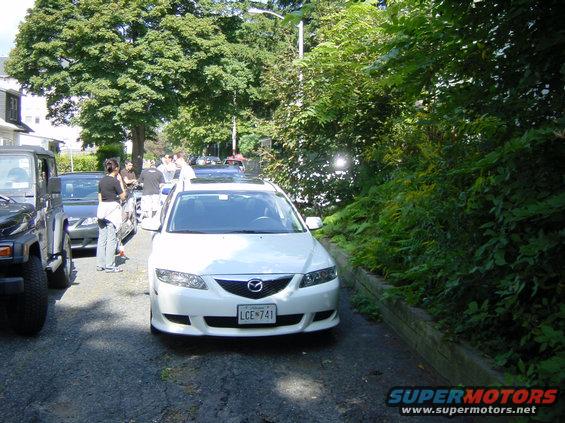 White Mazda 6 parked on asphalt, front view. License plate LCE 741. Jeep Wrangler to the left