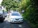 2003 Mazda 6 - A white Mazda 6 is parked on a street with trees and foliage. Another vehicle is visible to the left.
