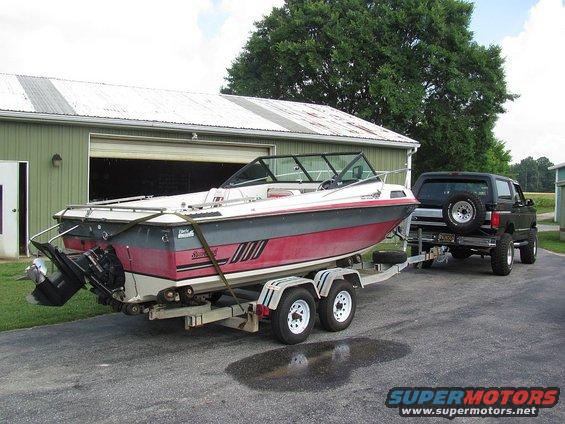 Black SUV towing a red and white boat on a trailer in front of a garage