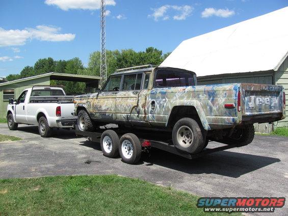 Jeep J-10 pickup truck on trailer being towed by white Ford pickup