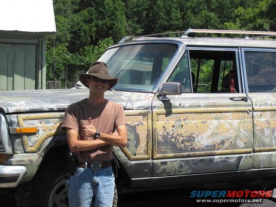 Weathered 1986 Jeep Grand Wagoneer, 3/4 front view, with a man giving a thumbs up