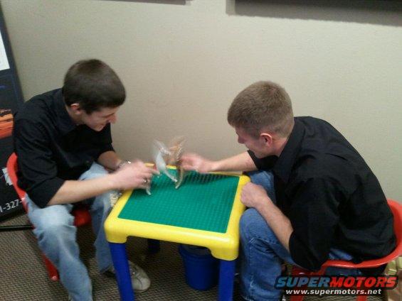 Two guys sit at a table playing with small toys