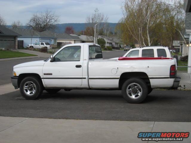White 1994 Dodge Ram pickup truck, side view, carrying a red-topped SUV