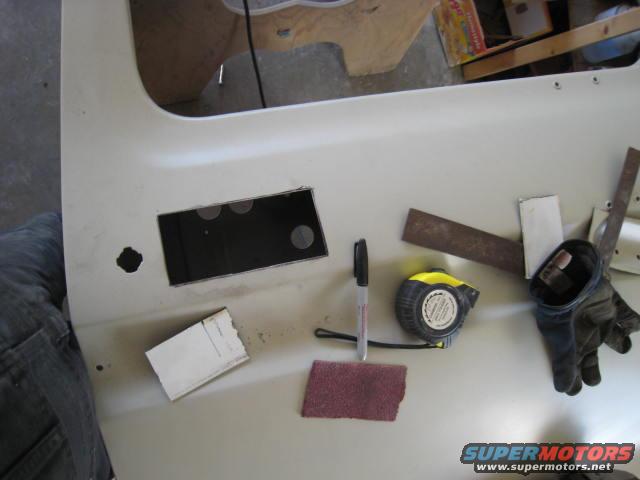 Close-up of a vehicle door panel with a cut-out, tape measure, marker, sandpaper, and gloves