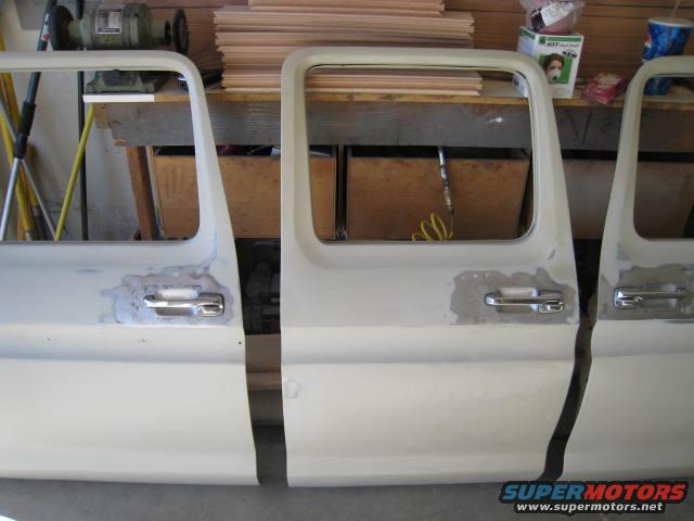 Three white truck doors, some with body filler, in a workshop
