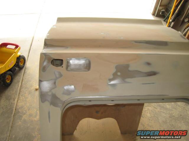 Truck door with body filler and primer, next to a yellow toy dump truck