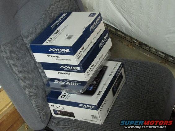 Stack of Alpine car stereo boxes on a gray patterned seat