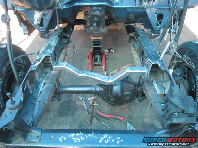 Truck frame with drivetrain components, jacked up. Some custom metalwork on the frame