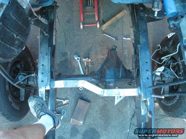 Truck frame with suspension and differential visible, under repair. A foot is in the lower left