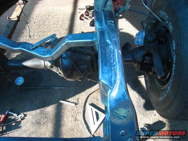 Truck frame with welded reinforcements and rear axle assembly, showing a tire with visible tread