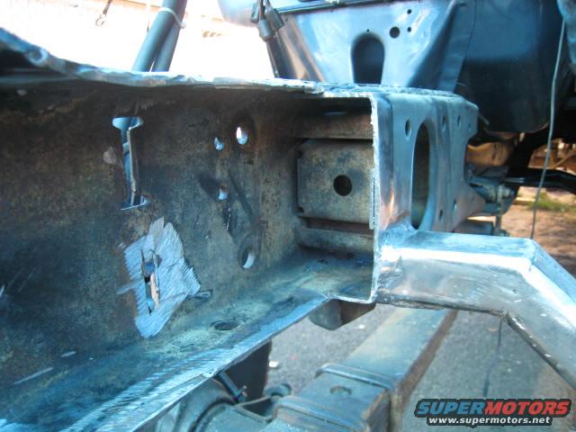 Close-up of a rusty truck frame with some new welds. Shows a leaf spring below