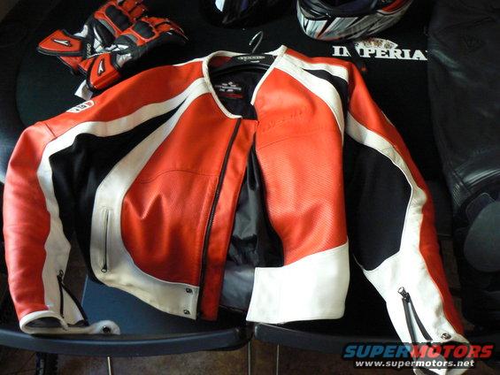Orange, white, and black leather motorcycle jacket with matching gloves and helmet in background