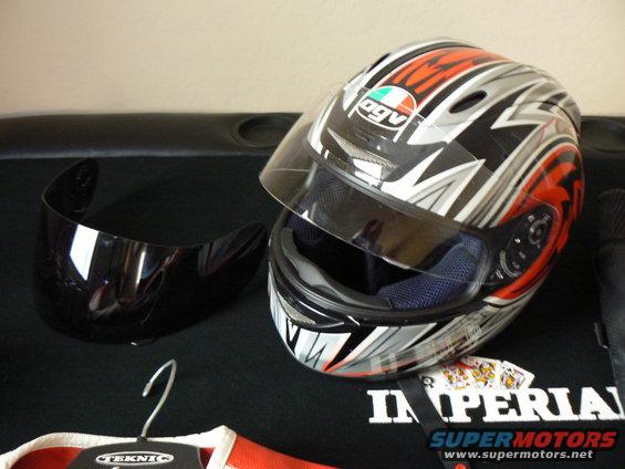 Motorcycle helmet with visor next to it, on a black surface. Some playing cards are visible underneath