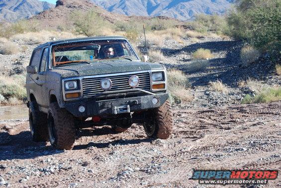 Green off-road SUV with aftermarket bumper and winch navigating rocky terrain