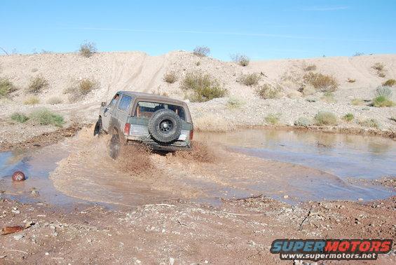 1980s Ford Bronco splashing through a mud puddle off-road