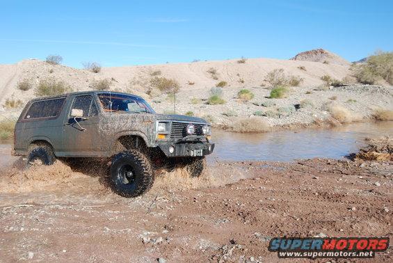Mud-covered green Ford Bronco driving through water and mud
