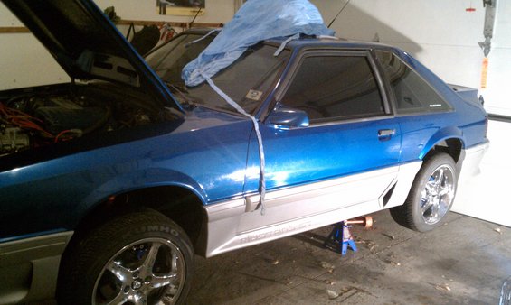 1990 Ford Mustang coupe, blue with silver trim, hood open, on jack stands. Another car is visible behind it