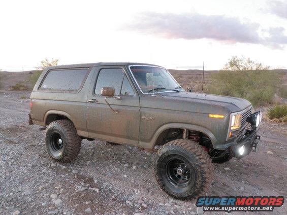Muddy, lifted Ford Bronco parked on a gravelly, desert-like terrain