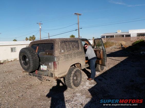 Mud-covered Ford Bronco with spare tire on rear, driver's door open, person entering