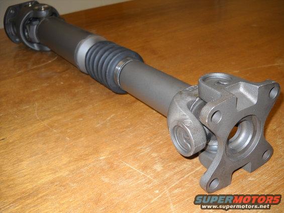 Driveshaft with U-joints and a flange on a wooden surface. SuperMotors logo visible