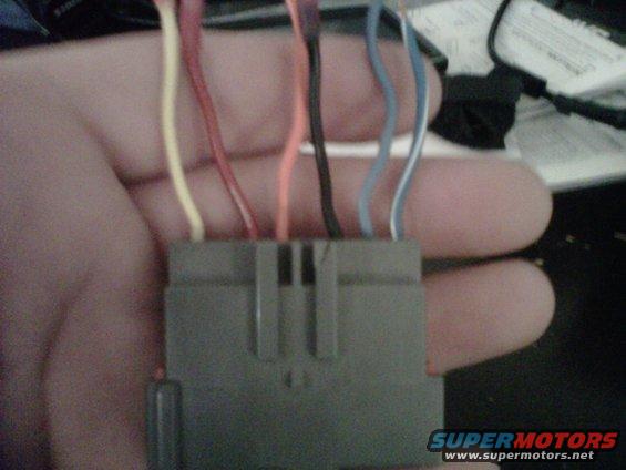 Close-up of a gray wiring harness connector with multiple colored wires extending from it, held by a hand
